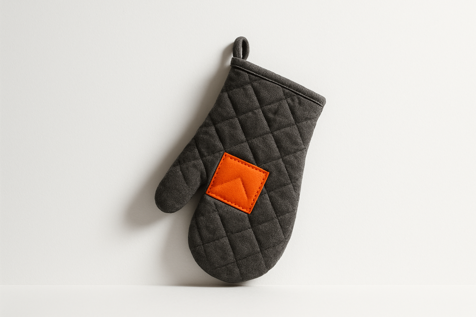 Charcoal grey quilted oven mitt with orange palm patch, symbolizing moving from ai governance to ai growth